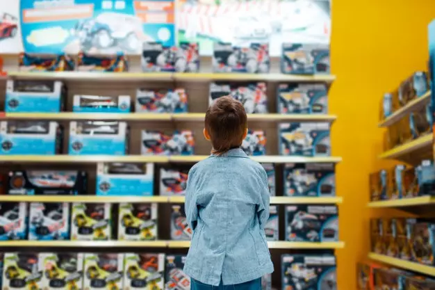 Garoto na prateleira da loja de crianças escolhendo brinquedos. Foto: Freepik