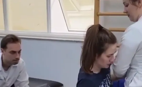 Eduarda, de 23 anos, faz fisioterapia com dois profissionais em um espaço de reabilitação